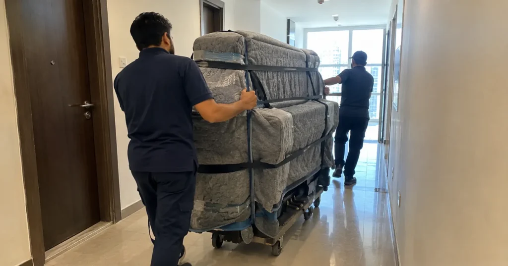 Moving a piano in Dubai movers rolling a wrapped upright piano